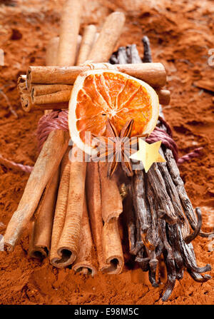 Bundle cinnamon and a bunch of vanilla beans with dried orange fruits on a brown cacao background. With a golden star and anise. Stock Photo