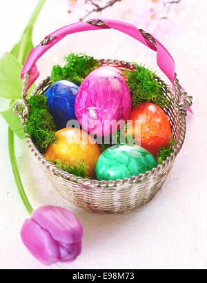 A basket full of colourful dyed marbled Easter eggs with a pretty pink tulip Stock Photo