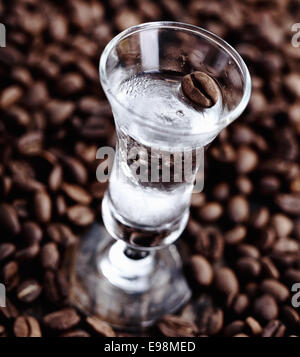 Clear coffee sambuca in a tall glass surronded by unground beans Stock Photo