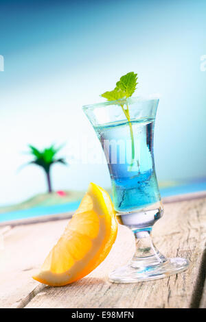 Blue Curacao Beach Cocktail with fresh lemon standing on a landing stage, with the pacific and a lagoon with a palm in the background. More Drinks in my portofolio. Stock Photo