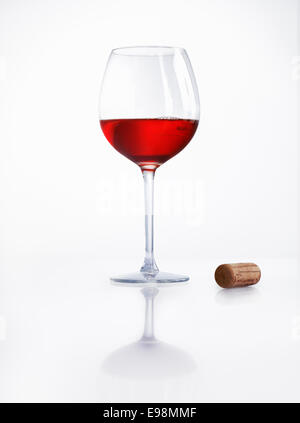 Glass half filled with red wine on a reflective white surface with a cork alongside at a party or celebration Stock Photo