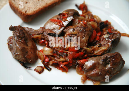 Pan fried chicken livers with caramelised onions and red peppers served on white plate with brown and rye bread and basil Stock Photo