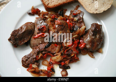 Pan fried chicken livers with caramelised onions and red peppers served on white plate with brown and rye bread and basil Stock Photo