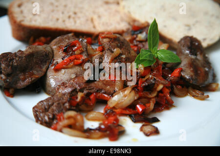 Pan fried chicken livers with caramelised onions and red peppers served on white plate with brown and rye bread and basil Stock Photo