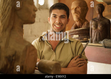 Portrait of man working, young student in art class, learning crafts profession, working with wooden statue and looking at camer Stock Photo