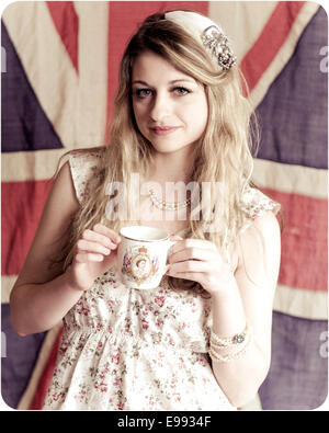 vintage looking photo of a young lady holding a coronation tea cup in front of a vintage union jack flag. with vintage hair Stock Photo