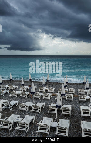 White reclining chairs on deserted beach during bad weather with dark, menacing rain clouds over the sea Stock Photo