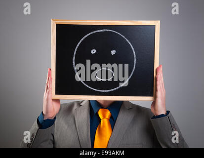 Businessman hiding his face with a white billboard with a surprised face on it Stock Photo