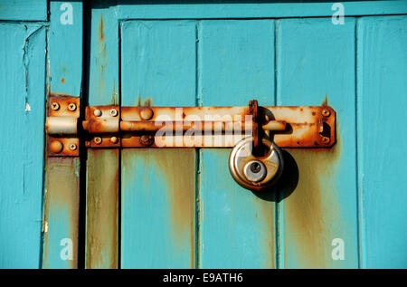 Rusty padlock on hinges with peeling turquoise painted door Stock Photo