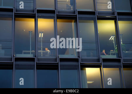Office workers at desks behind modern glass facade, Rheinauhafen, Cologne, North Rhine-Westphalia, Germany Stock Photo