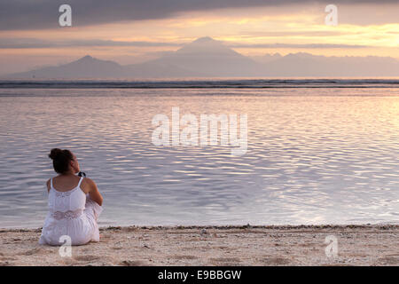 Woman sitting on sand beach watching sunset over sea, view of Bali from 'Gili Trawangan', 'Gili Island', Indonesia