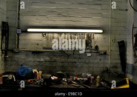 A fluorescent strip light illuminates spanners on a rack and scattered tools on a workbench Stock Photo