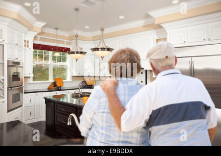 Happy Senior Couple Looking Over Beautiful Custom Kitchen Design. Stock Photo