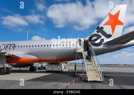 Jetstar A320 at Christchurch Airport. Single passenger boarding a Jetstar plane using a boarding ramp boarding stairs