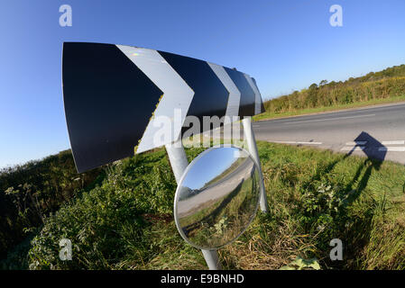 warning sign of sharp bend and circular safety mirror to give drivers emerging from junction view of road uk Stock Photo