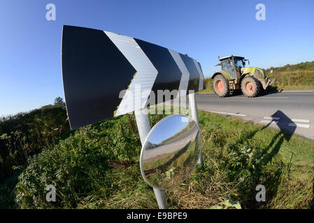 tractor passing warning sign of sharp bend and circular safety mirror to give drivers emerging from junction view of road uk Stock Photo
