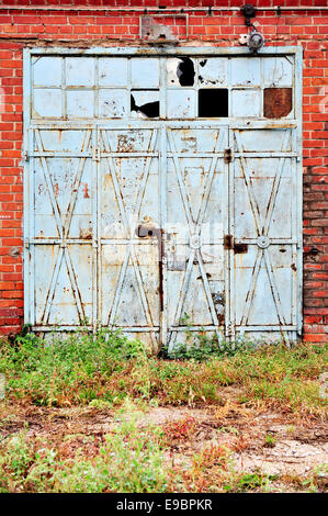 Old and rusty blue iron gate from an abandoned brick warehouse Stock Photo