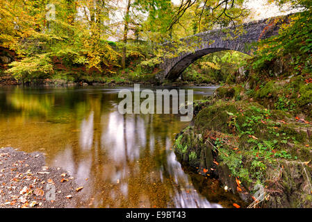 Autumn time and a slow moving river flows under an old stone bridge near Ambleside in the Lake District National Park, Cumbria Stock Photo