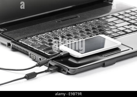 Data transfer between devices. Close up shot of mobile phone connected to a laptop with a usb cable, isolated on white background. Stock Photo