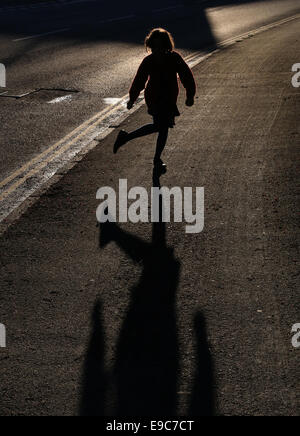 young girl dancing at roadside silhouetted by striking bright low evening sun on a pavement, with a long shadow and backlit hair Stock Photo