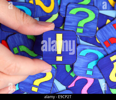 Woman's hand hold red exclamation mark with background of question marks. Marks drawn by me. Stock Photo