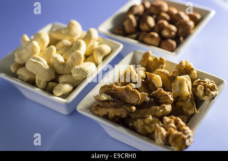 Small white snack bowls filled with a different type of nut. Cashews, walnuts and hazelnuts. Stock Photo