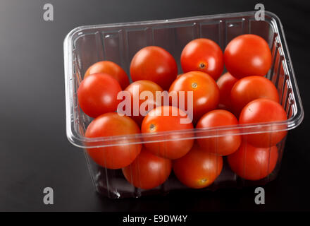 Fresh cherry tomatoes in plastic container on black background. Stock Photo