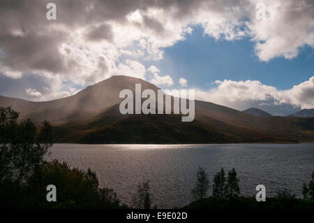 Looking across Loch Quoich at Gairich, a Munro, in the rain with sunrays through the clouds. Stock Photo
