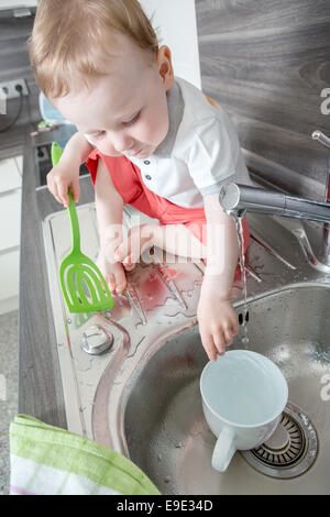 Portrait of a 7-8 years old boy washing the dishes at home. Child help ...
