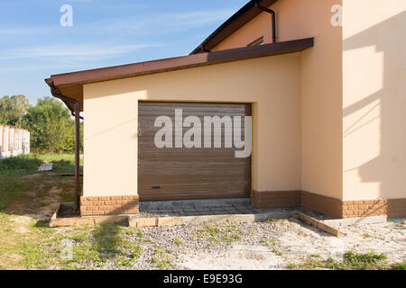 Newly built single garage with a closed roll up door annexed to the edge of a new house construction Stock Photo