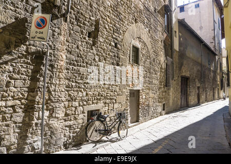 view down narrow side street of lovely old stone wall whose surface & blocked up Romanesque arches tell a story of decline Stock Photo