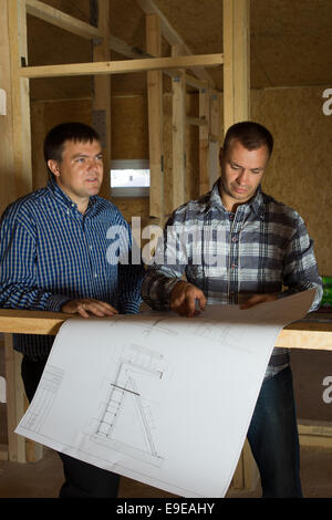 Two builders checking a blueprint together as they standing inside a half constructed timber frame house Stock Photo