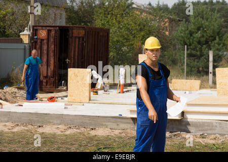Workman pointing to something on the ground as he stands in his overalls and hardhat holding a document on a building site for a Stock Photo
