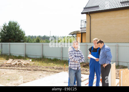 Group of builders and site engineers standing discussing details on a cleared residential plot on the foundation of a new house Stock Photo