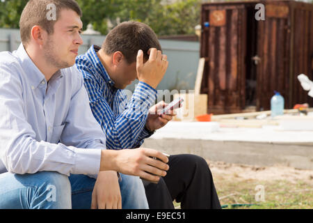 Close up Site Engineers Sitting at the Corner, One is Busy with Phone and the Other is Having a Cup of Coffee. Stock Photo