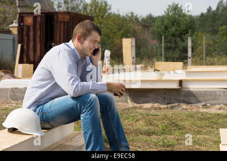 Young Handsome Male Engineer Talking Someone Through Mobile Phone with White Helmet on the Side. Stock Photo