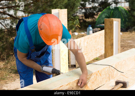 Workman drilling a hole in a wooden clad insulated beam on a new build construction site for a new house Stock Photo