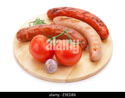 Various grilled sausages with condiments and tomatoes on cutting board. Isolated on white background Stock Photo