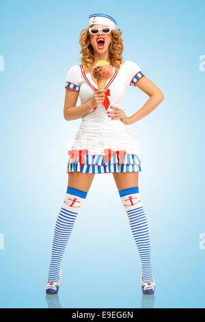 Creative retro photo of a fashionable pin-up sailor girl, holding an ice cream in a waffle cone and screaming on blue background Stock Photo