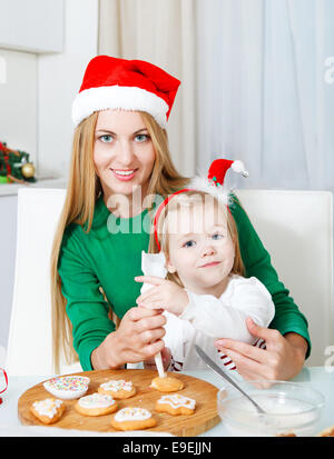 Adorable little girl with her mother baking Christmas cookies at the kitchen Stock Photo