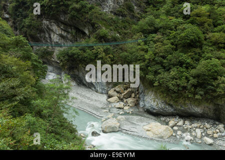Lush forest, steep cliff and suspension bridge over a rocky river at the Taroko National Park in Taiwan Stock Photo