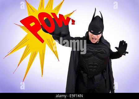 a man in a comedy batman costume punches the air with a giant POW sign, like the classic tv show Stock Photo