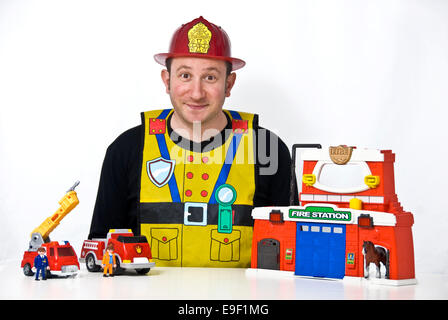 a man dressed in a child's fireman outfit and toys Stock Photo