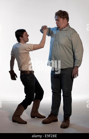 two men in the cowboy wild west era acting out scenes from of mice and men, dressed in period costume clothes while one punches Stock Photo