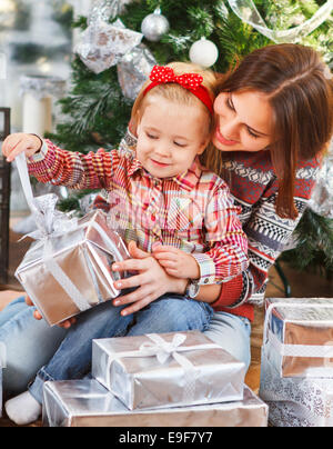 Two happy sisters opening Christmas presents sitting by the Christmas tree Stock Photo