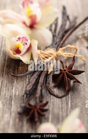 Tied vanilla pods and orchid flowers on old wooden table. Stock Photo