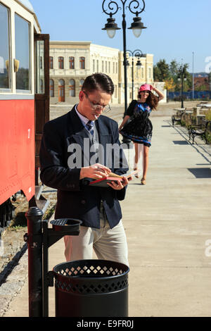 Romantic scene with man by the train reading book and retro woman running towards him on train station Stock Photo