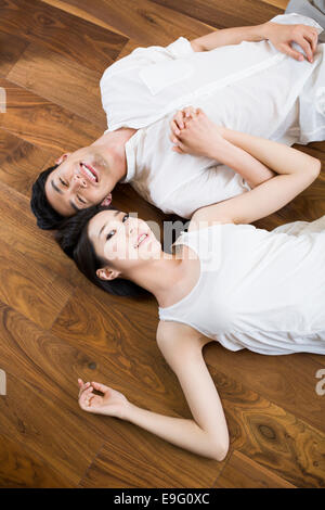 Young couple holding hands lying on wooden floor Stock Photo