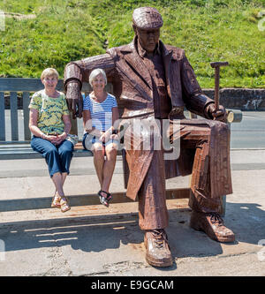 A giant metal man sat on a bench with two ladies alongside him Stock Photo