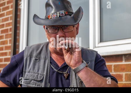 An elderly man in a leather cowboy hat smoking a cigarette Stock Photo